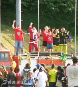 Santa and his helpers hitch a ride with a fire truck.