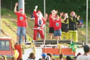 Santa and his helpers hitch a ride with a fire truck.