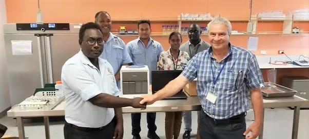 Front – MHMS Dr Gregory Jilini receiving the GeneXpert Machine and the laptop from WHO, Dr. Magdi Kassem with a handshake. Witnessing the handover were the Director of National Public Health laboratory, Mr. Dickson Manongi, Mr. Oliver Lukos (Medical Lab Technologist) and WHO staff; Ms Lanique Pitasua and Mr. Robinson Minevaleke at the back.