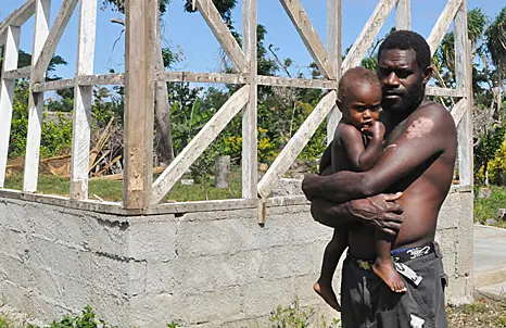 Christopher Nipo with his youngest son, behind them, what remains of their home, destroyed by Tropical Cyclone Pam