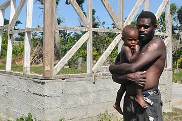 Christopher Nipo with his youngest son, behind them, what remains of their home, destroyed by Tropical Cyclone Pam