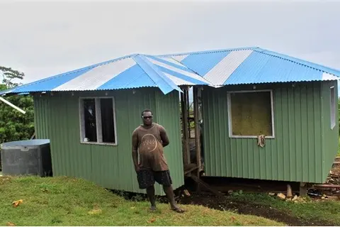Eddie Voko in-front of his new permanent home that he build through money acquired from shallot sales. The home is in construction phase and is nearing completion.