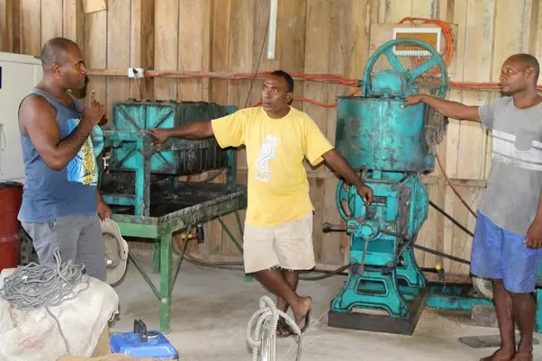 Policy Secretary of the Productive Sector Dr. Samson Viulu from the government’s policy unit discusses with workers of a coconut milling station in Poro village.